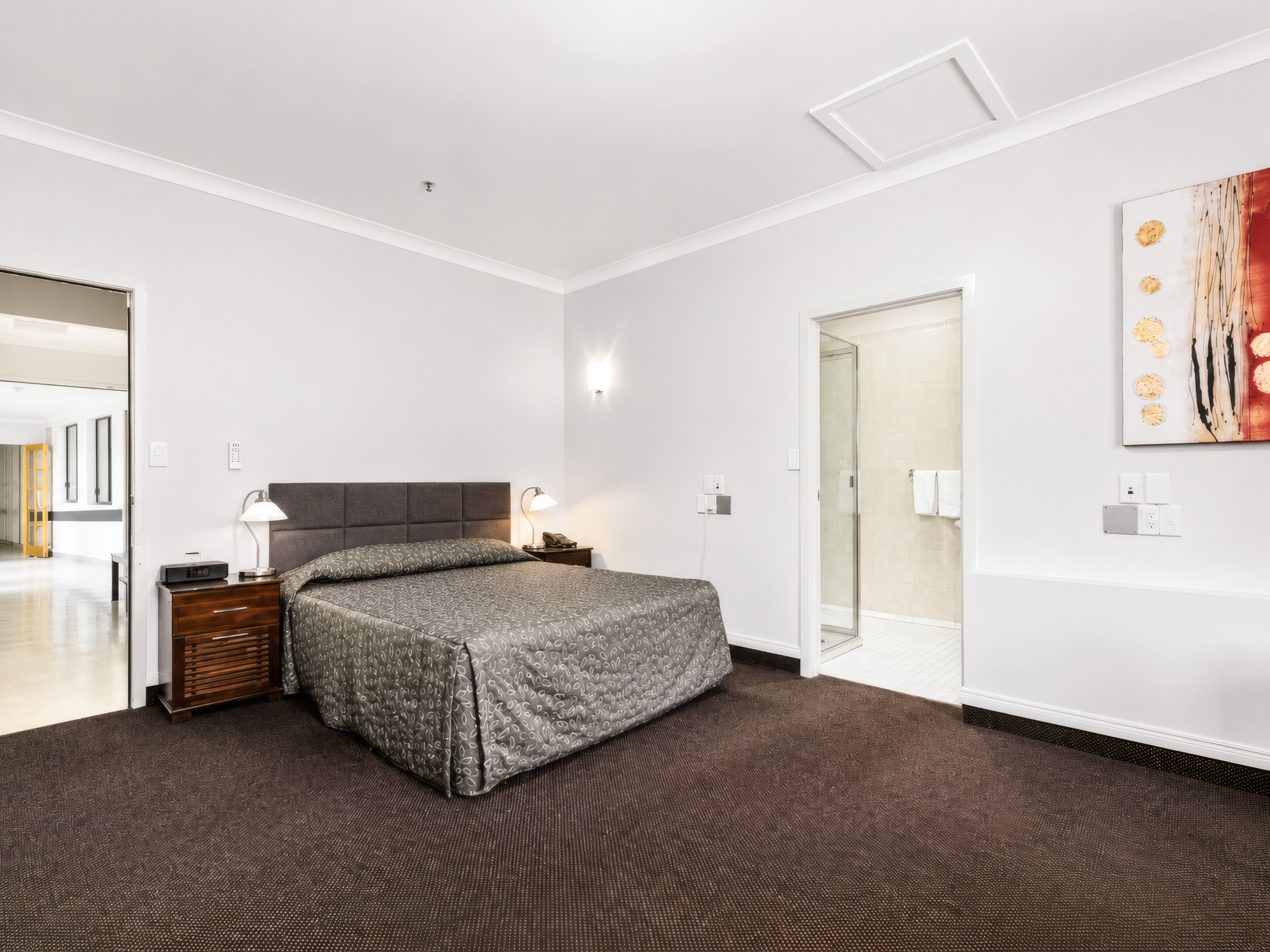 A hotel room with a bed, bedside table, lamp, and a painting on the wall.