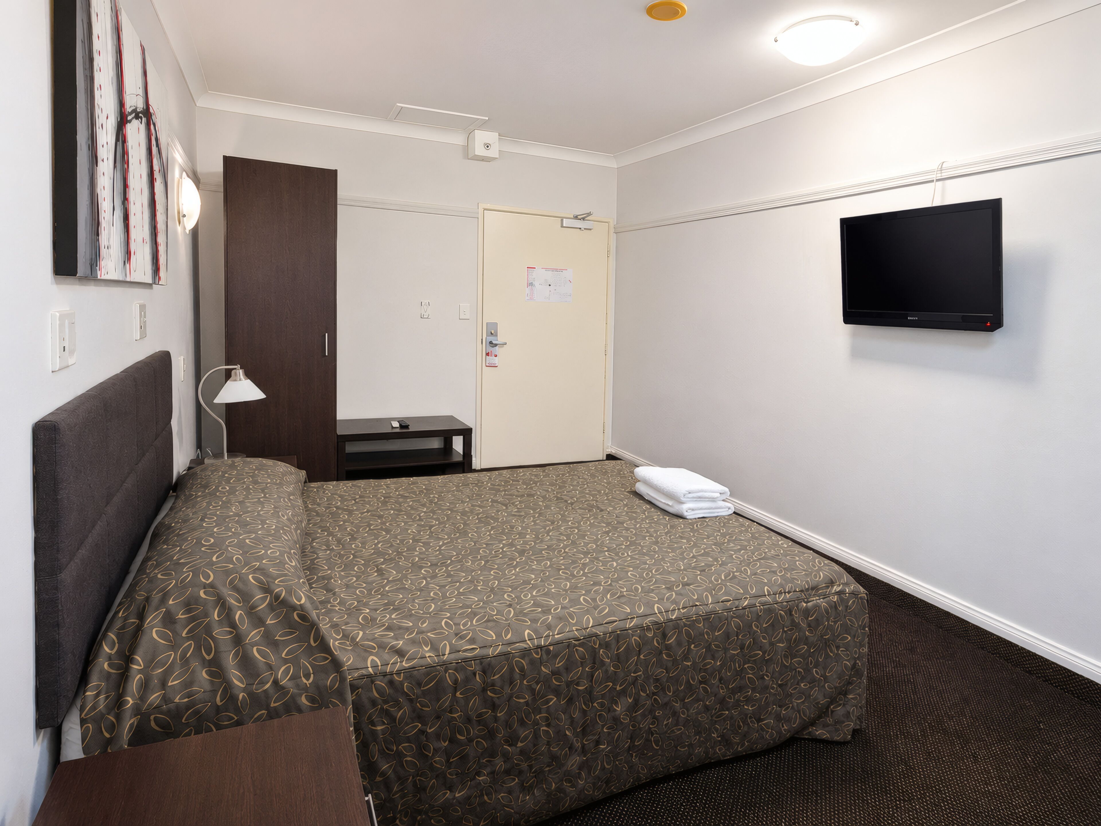 Een hotelkamer met een bed, een televisie, een bureau en een deur.