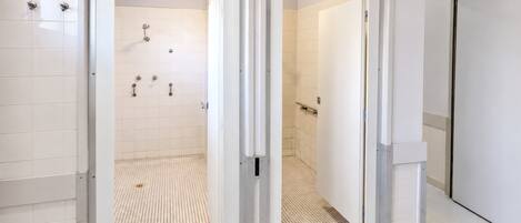 Un baño moderno con azulejos blancos, zona de ducha con suelo de rejilla y una puerta que da a otra habitación.