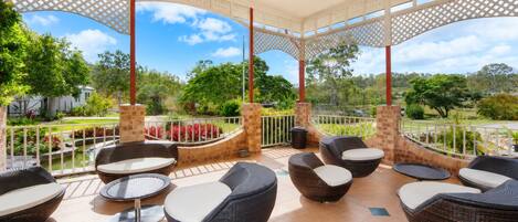 A covered outdoor seating area with wicker furniture and a view of a landscaped garden.