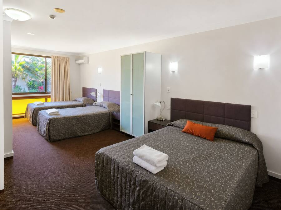 Ett hotellrum med två sängar, en garderob, ett nattduksbord och ett fönster med gardiner.