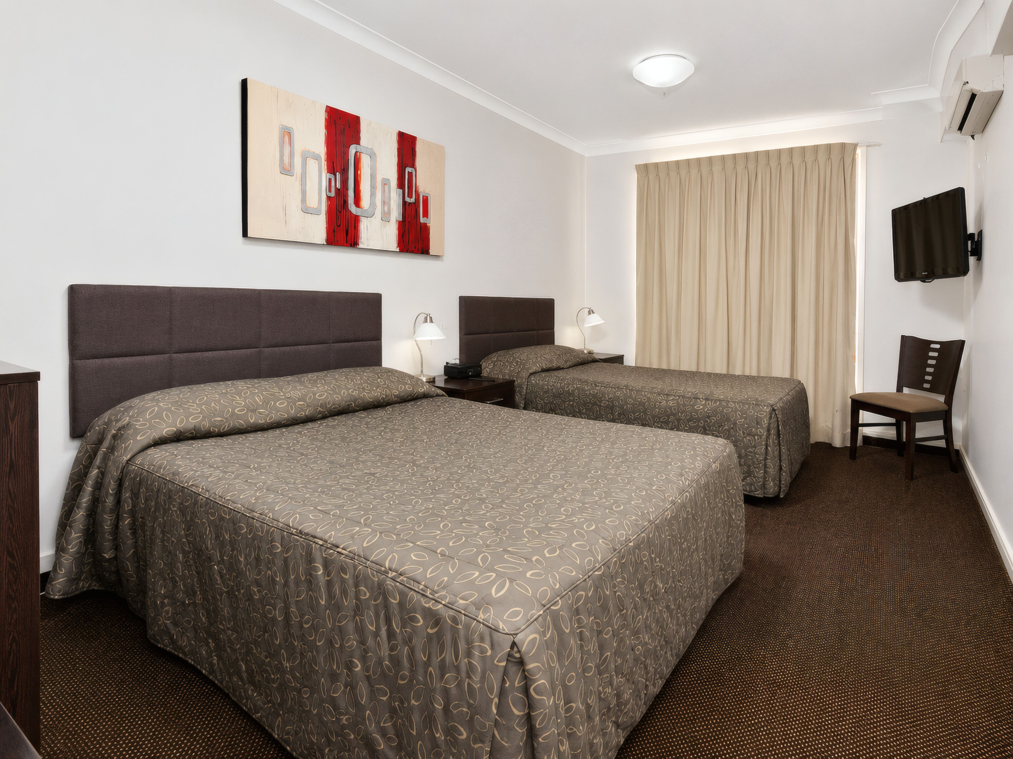 A hotel room with two beds, a TV, a chair, and a painting on the wall.