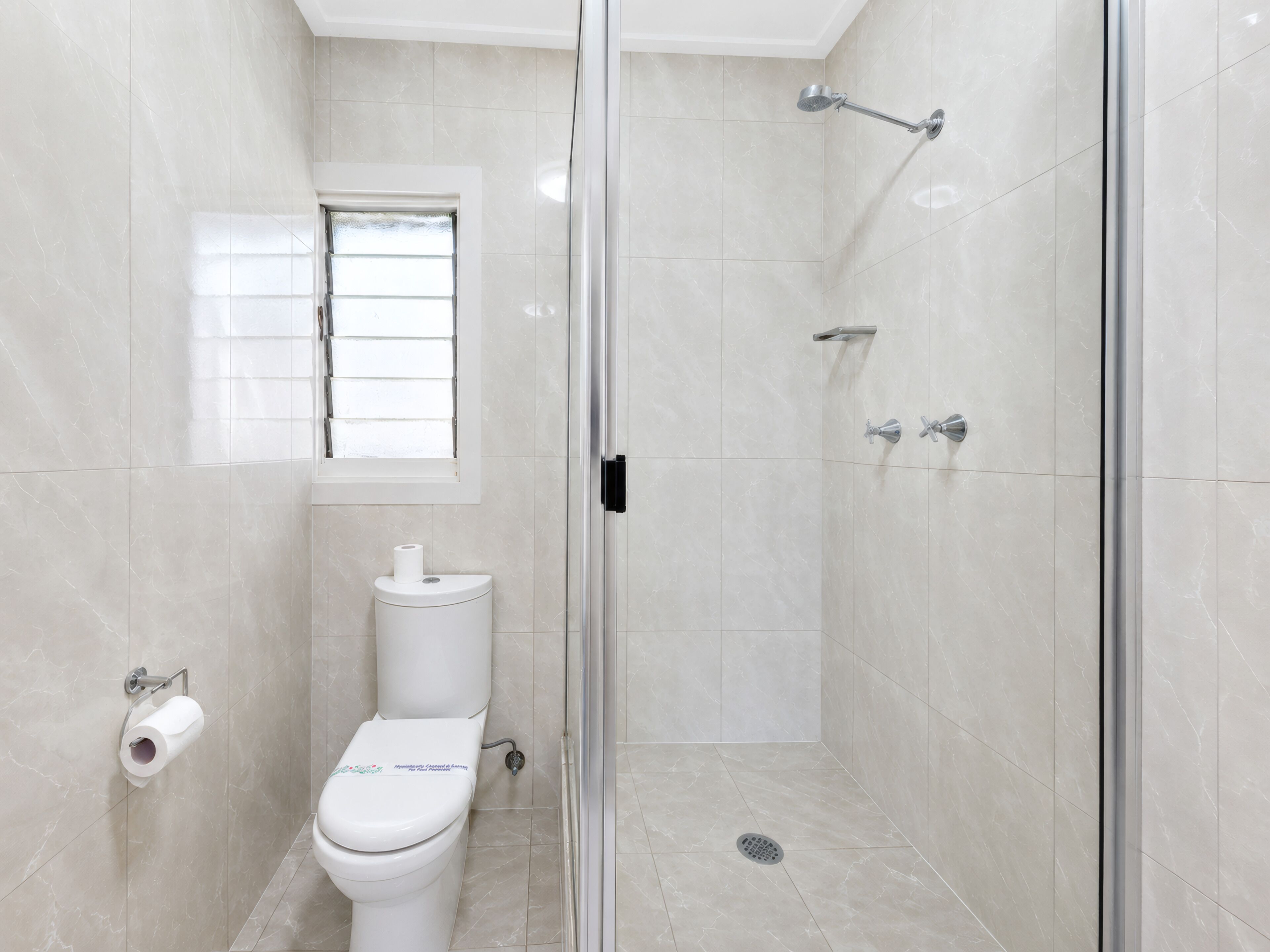 Un baño con inodoro, ducha con puerta de cristal y ventana.