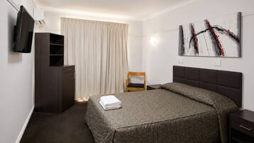 Une chambre d’hôtel avec un lit, une chaise, une armoire, un téléviseur à écran plat et un tableau au mur.