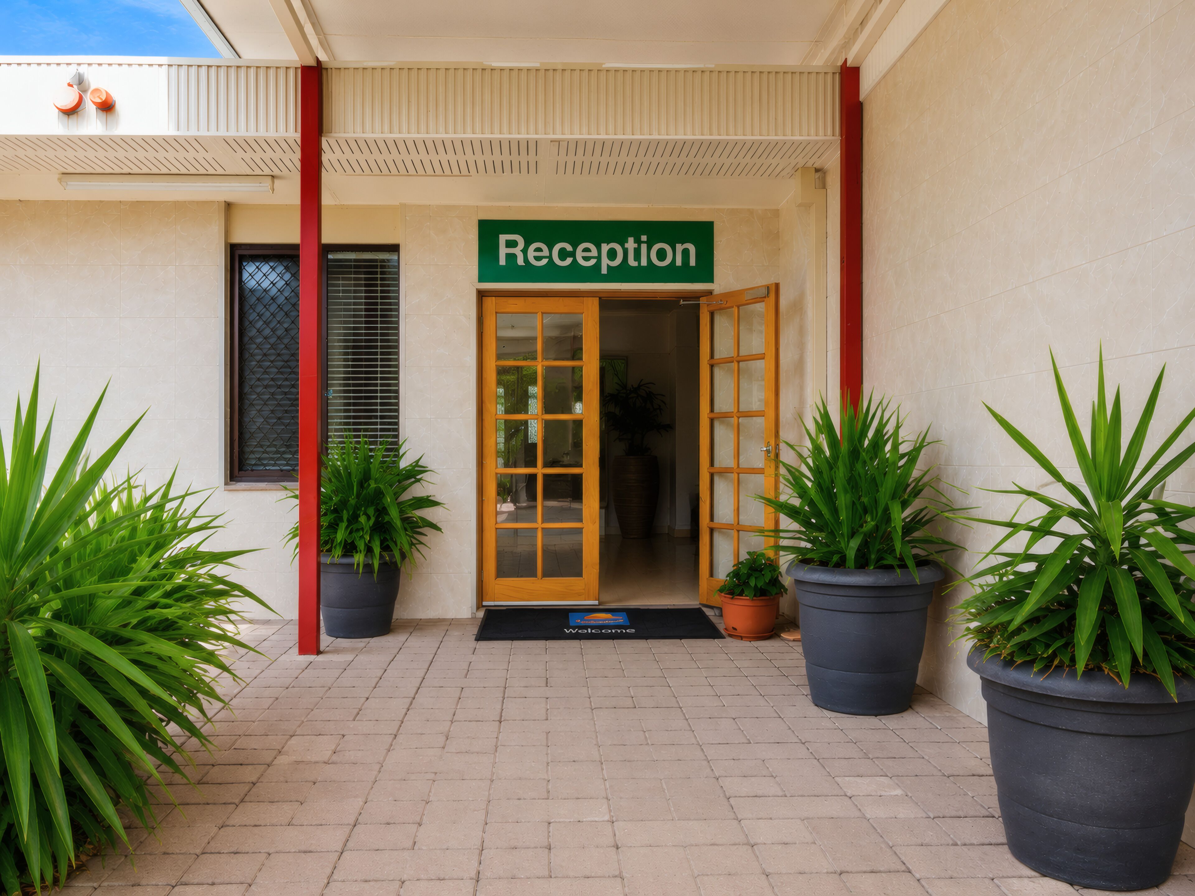 Un área de recepción con un letrero, una puerta de madera y plantas en macetas.
