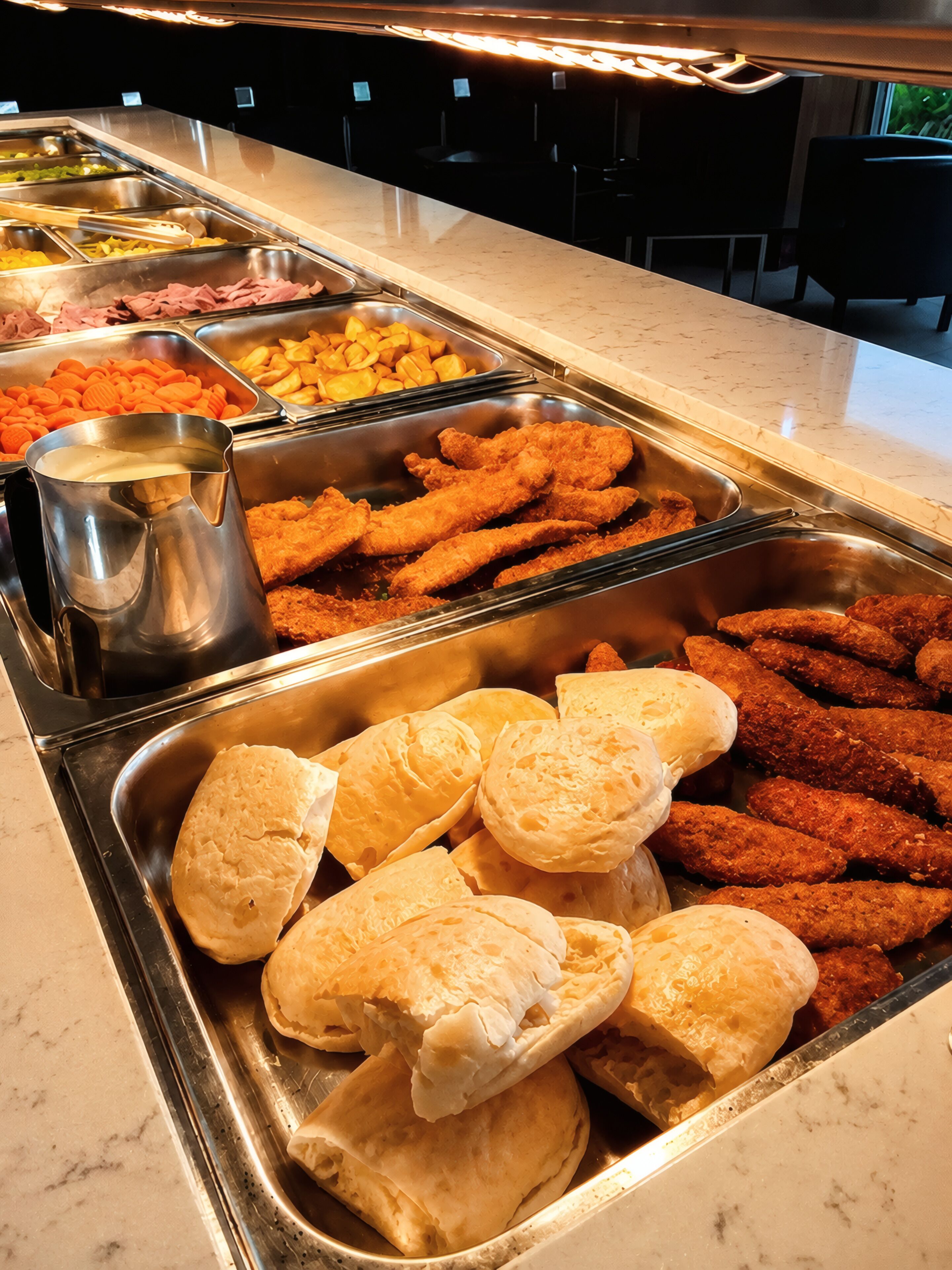 A buffet with various food options including breaded chicken, vegetables, and a beverage pitcher.