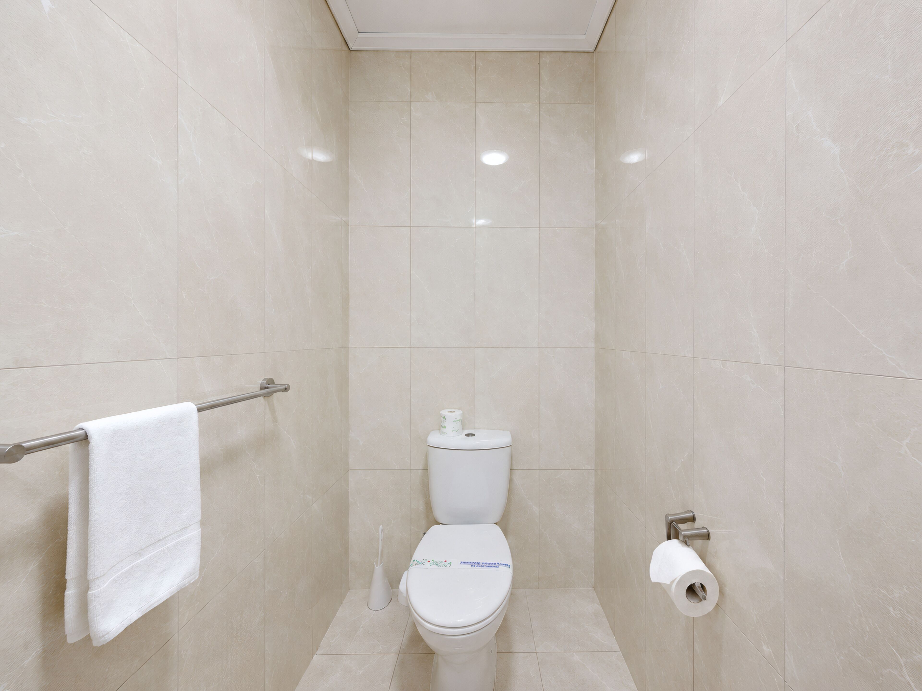 Une petite salle de bain moderne équipée de toilettes, d’un porte-serviettes et d’un support à papier toilette.