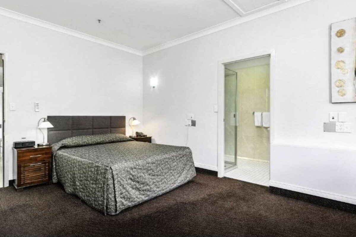 Ein Schlafzimmer mit einem Bett, einem Nachttisch, einer Lampe und einer Tür zu einem Badezimmer.
