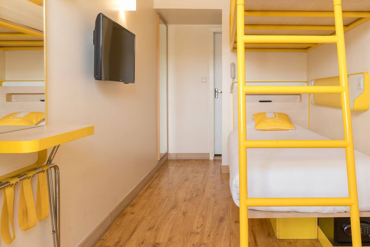 Een slaapkamer met stapelbedden, een televisie aan de muur, een spiegel en een deur naar een andere kamer.