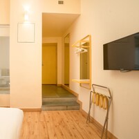 Una camera d'albergo con un letto, una TV a parete, uno specchio e un bagno visibile attraverso una porta aperta.