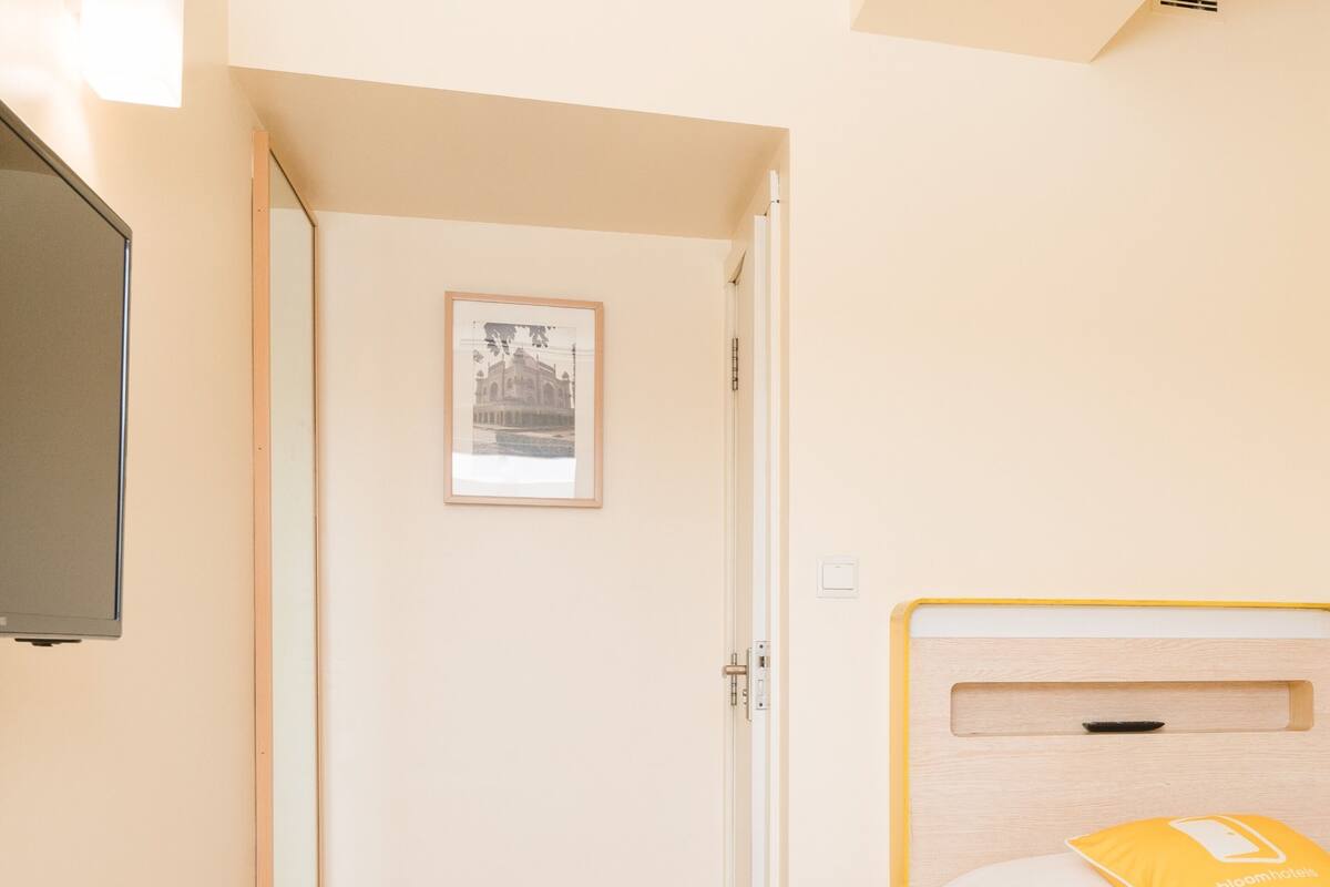 Een hotelkamer met een bed, nachtkastje, een aan de muur bevestigde televisie en een deur die naar een andere kamer leidt.