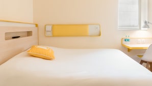 A hotel room with a bed, a bedside table with a lamp, a small desk, and a window with a view.