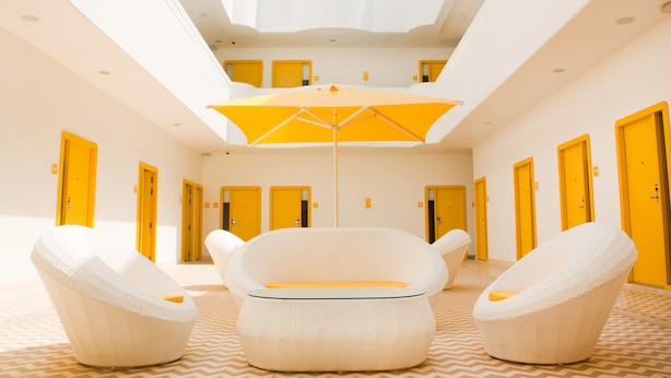 A hotel lobby with a high ceiling, yellow doors, and a central seating area with a large umbrella.