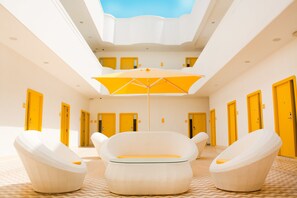 Un vestíbulo de hotel con techo alto, puertas amarillas y una zona de estar central con un gran paraguas.