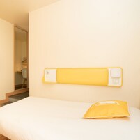 Een slaapkamer met een bed, een geel kussen en een stopcontact aan de muur.