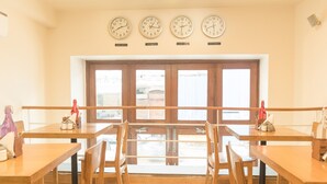 A dining area with wooden tables and chairs, a large window with a view, and four clocks on the wall.