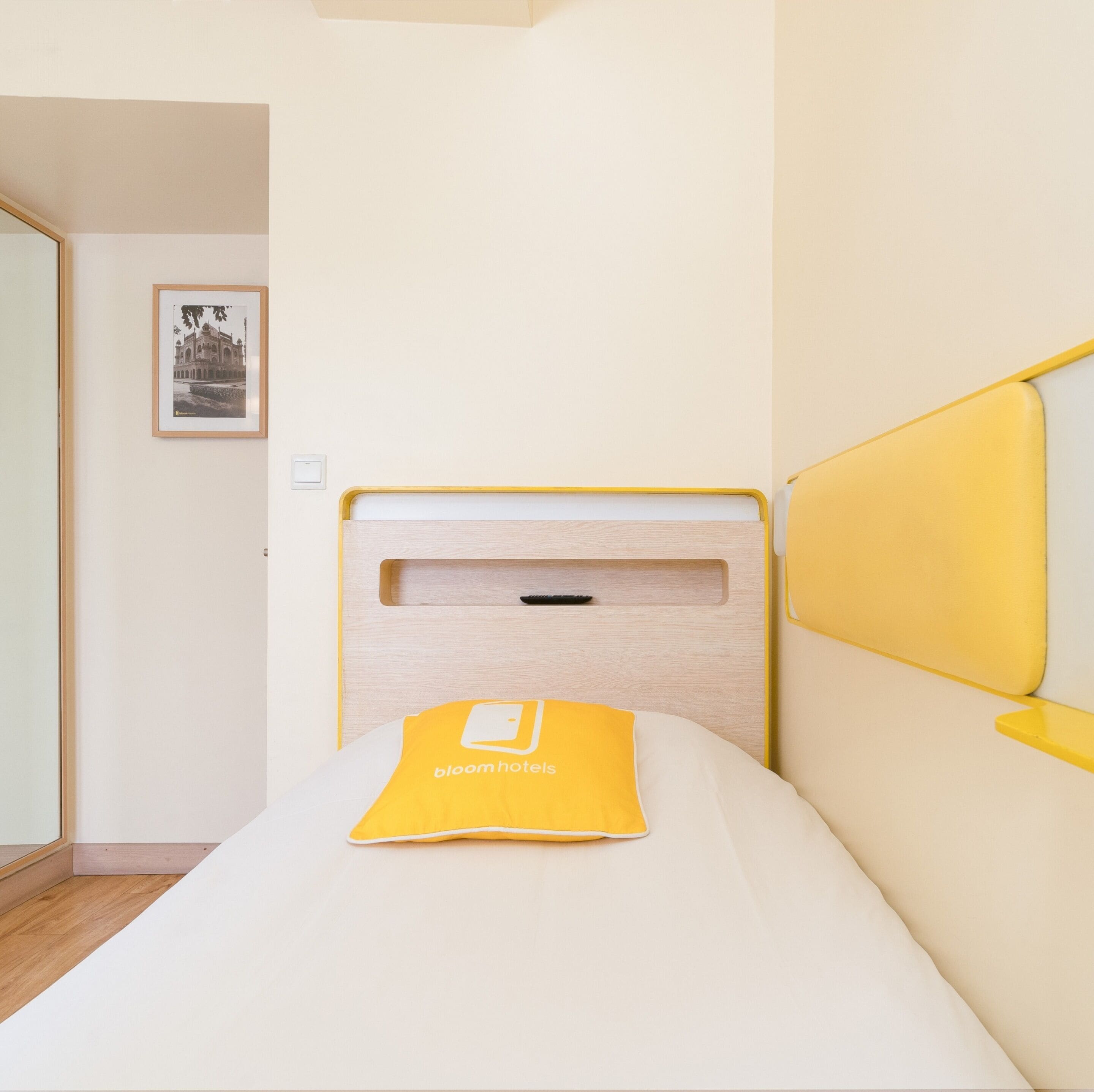 Una camera d'albergo con un letto, un comodino, un quadro appeso al muro e un pavimento in legno.