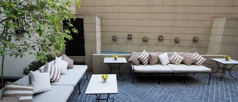 An outdoor patio with a sofa, two tables, and a decorative wall with water spouts.