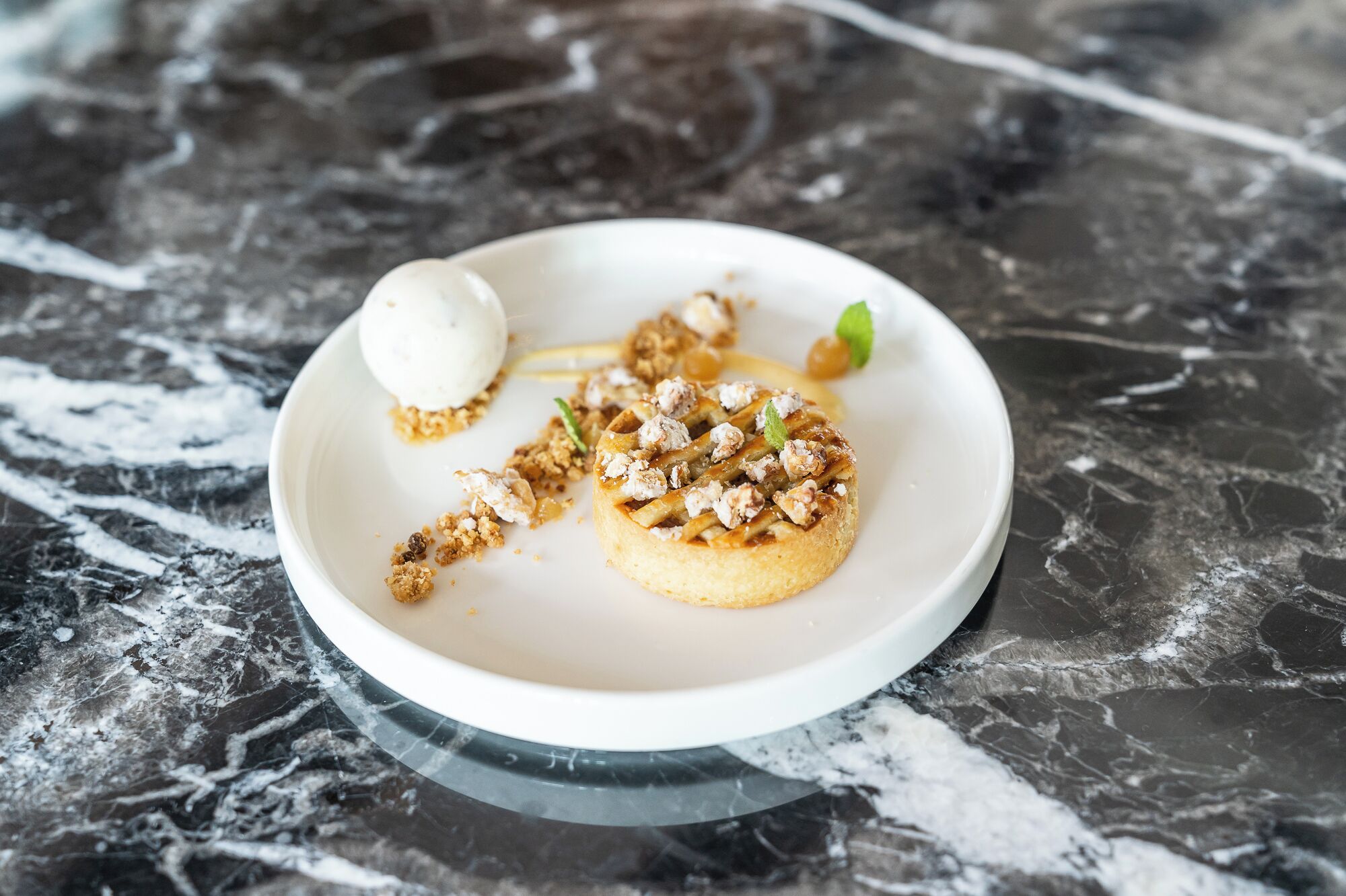 En desserttallrik med en våffla, nötter och en skopa glass, placerat på en marmoryta.