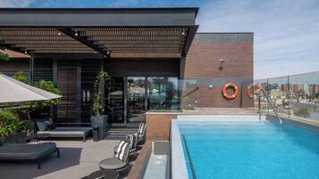 A rooftop pool area with a modern design, including a pool, lounge seating, and a covered patio.