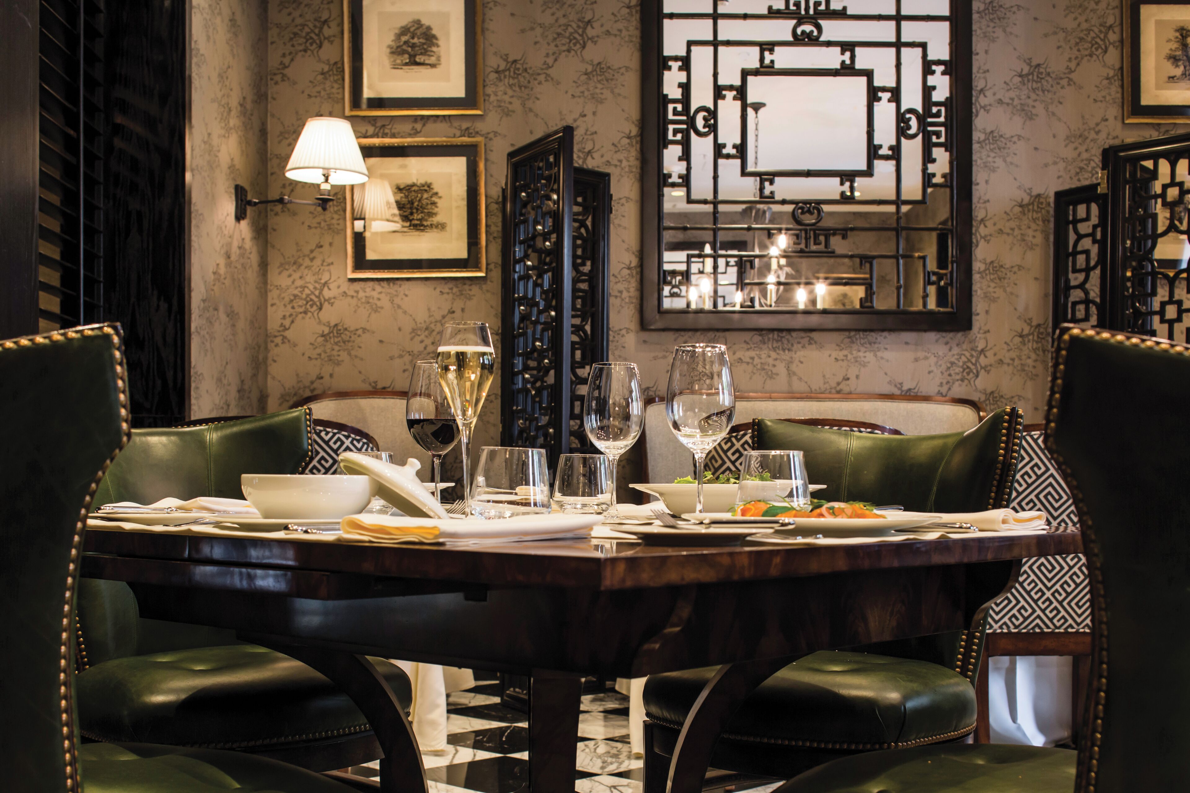 A dining area with a marble-tiled floor, a dark wooden table set for four, and green upholstered chairs.