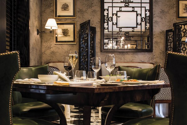 Comedor con piso de baldosas de mármol, una mesa de madera oscura dispuesta para cuatro personas y sillas tapizadas en verde.
