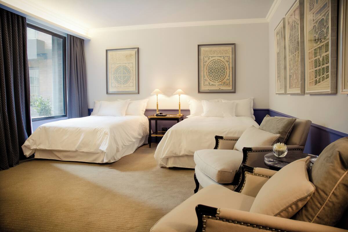 A hotel room with two beds, a sofa, a nightstand, and framed artwork on the walls.