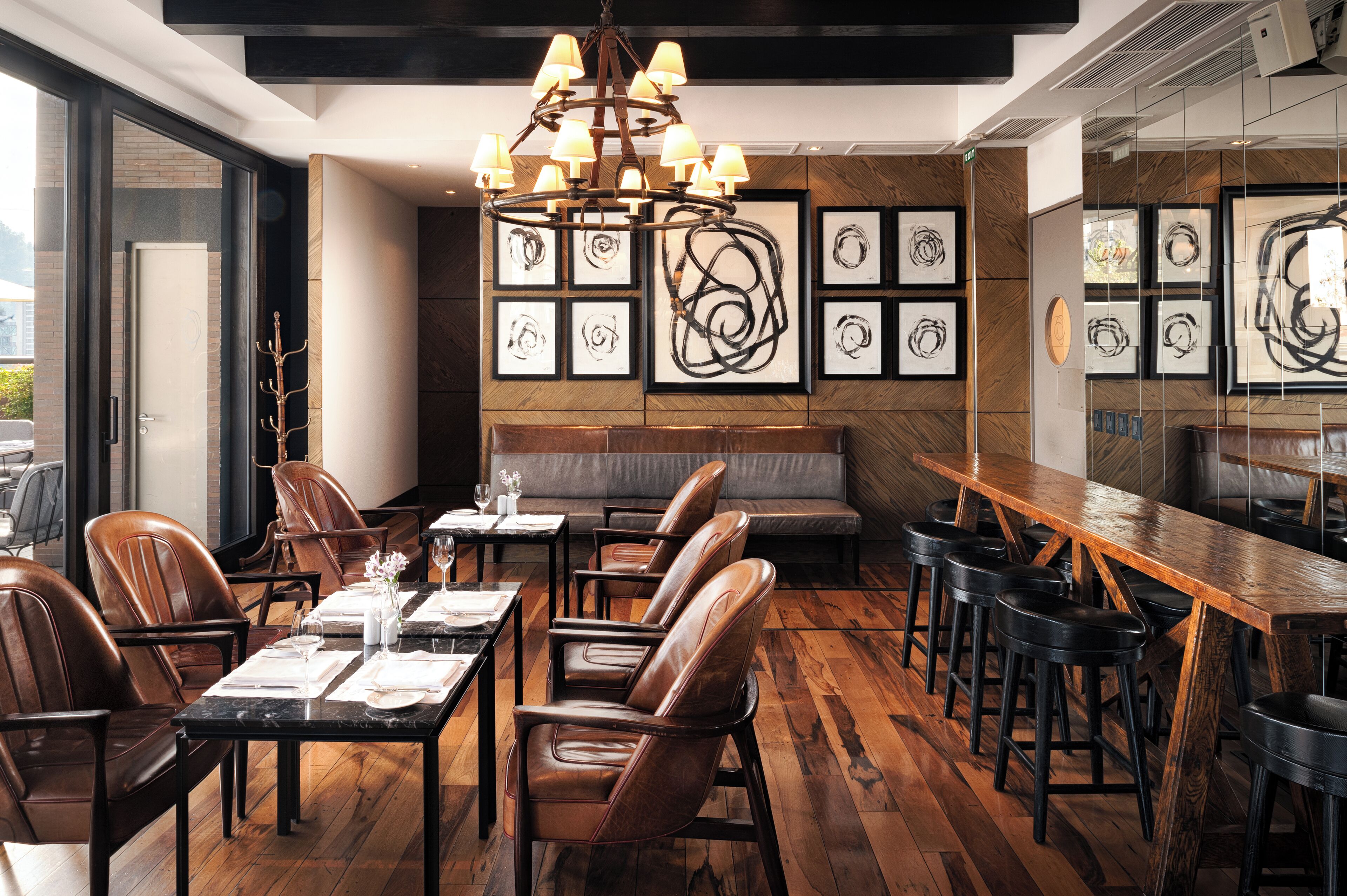 Un restaurante con suelo de madera, sillas de cuero, una barra larga de madera y una araña.