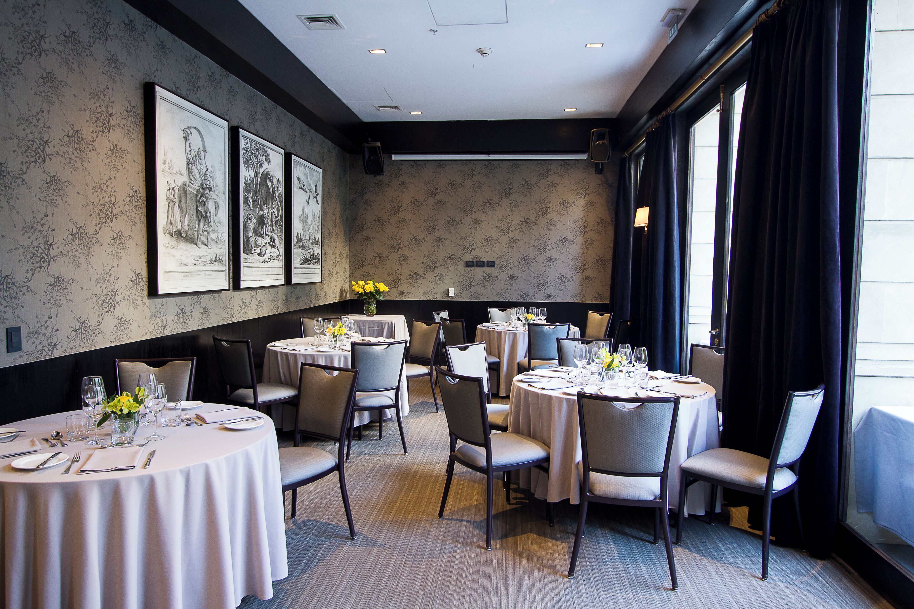 A dining area with round tables, chairs, and framed artwork on the walls.