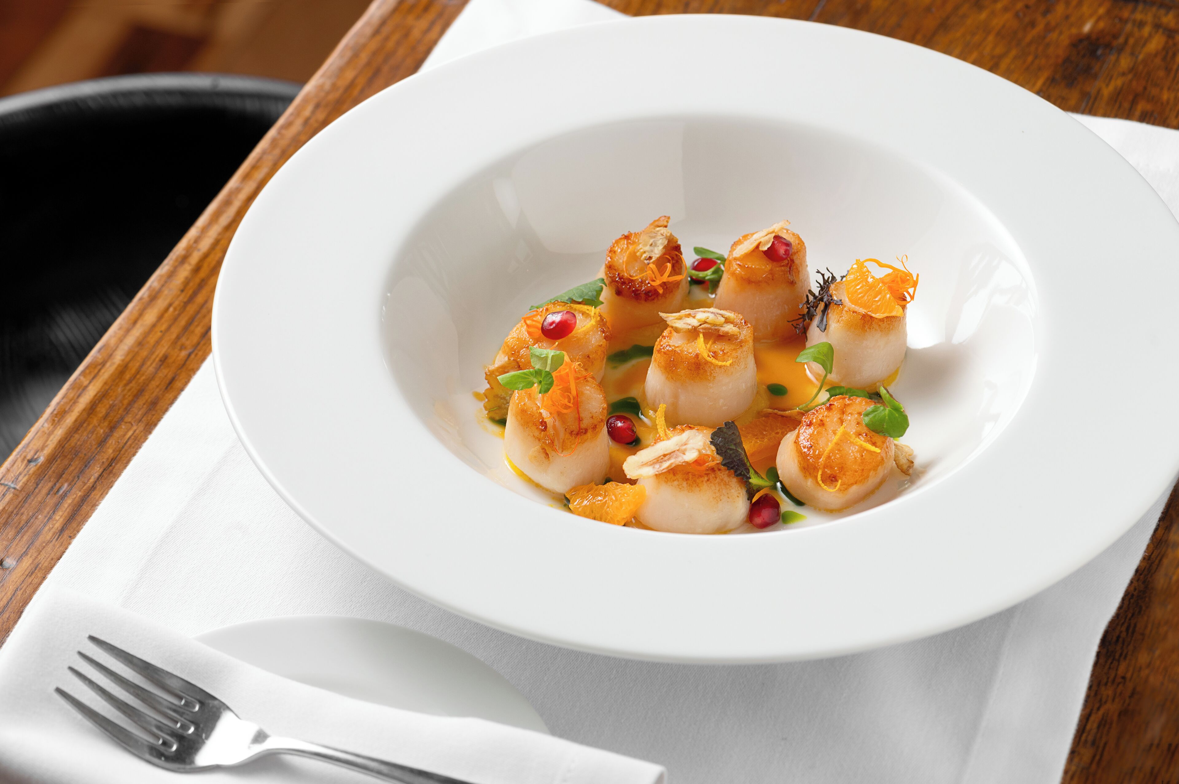 A white plate with scallops and garnishes on a wooden table.