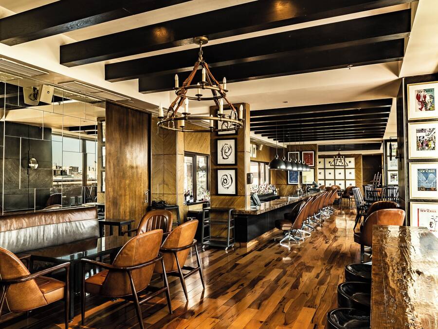 A bar area with wooden flooring, leather chairs, and a long counter.