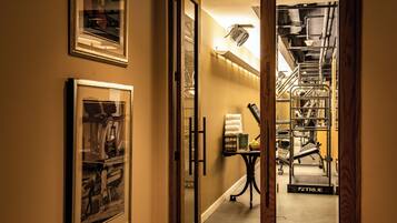 A hallway leading to a gym with exercise equipment, framed pictures on the walls, and a small table with towels.