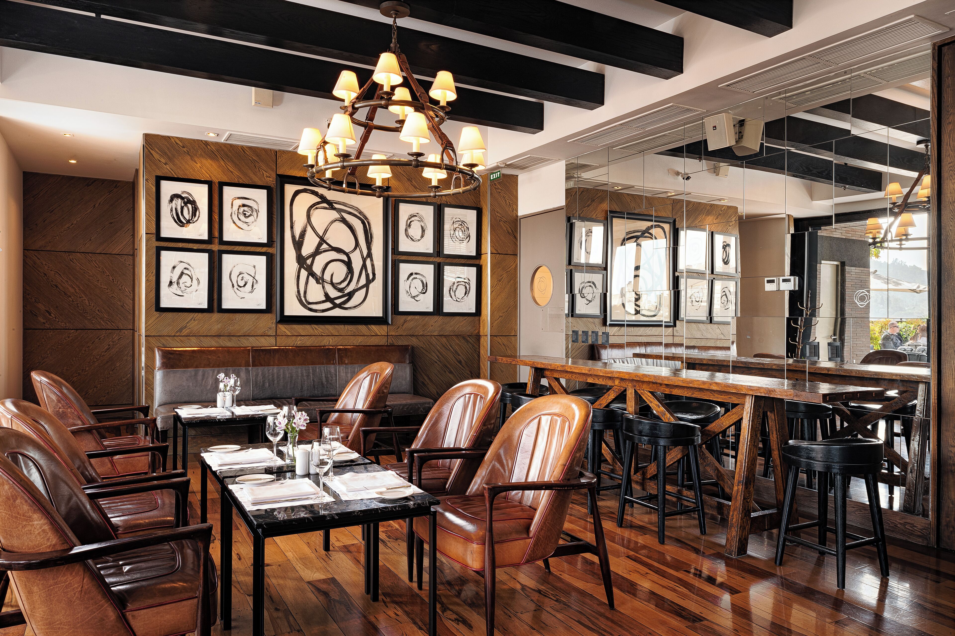 A restaurant interior with wooden flooring, leather chairs, a central dining table, and artwork on the walls.