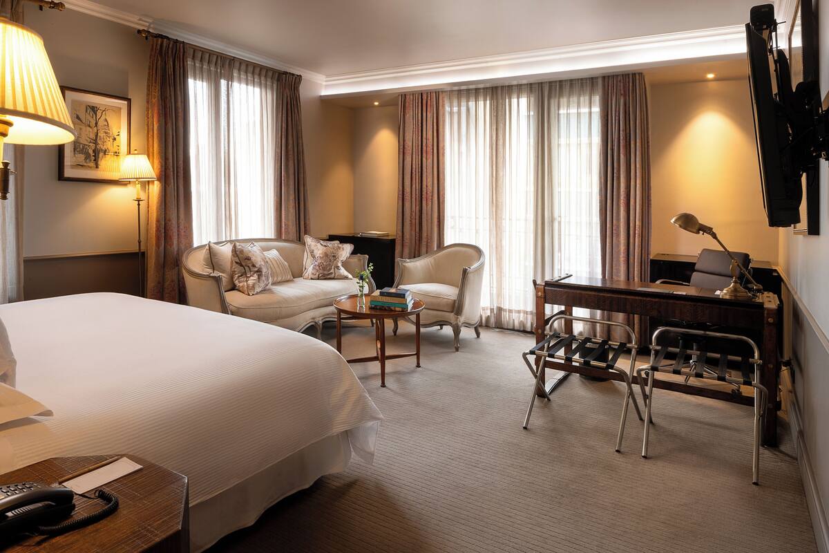A hotel room with a large bed, a sofa, a desk with a chair, and a lamp.
