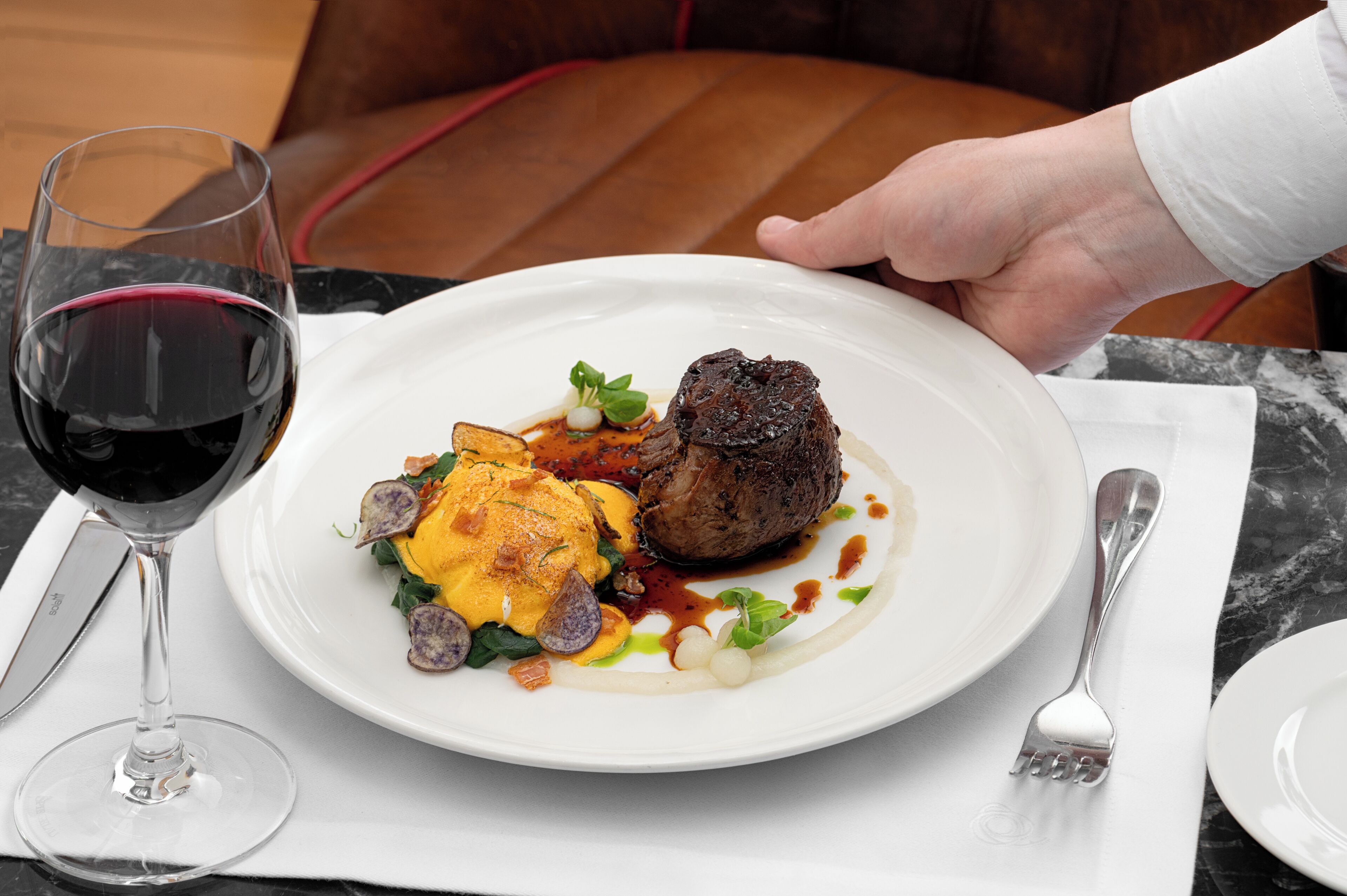 A plate of food with a glass of red wine on a table.