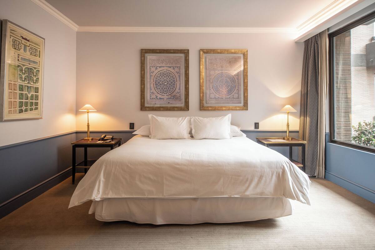 A neatly made bed with white linens, two framed calligraphy pieces on the wall, and two bedside lamps.