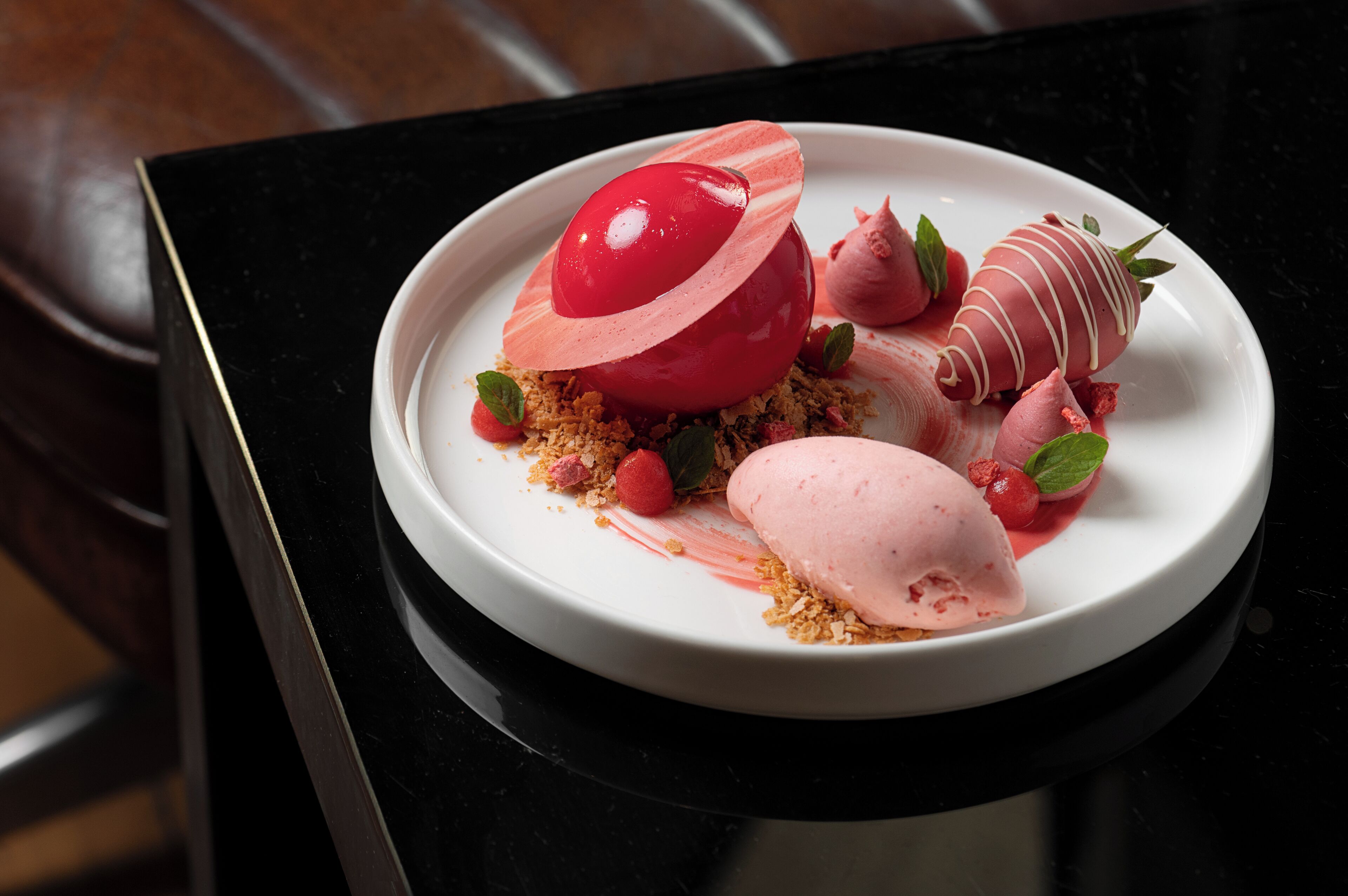 A dessert plate with a red and pink dessert, garnished with mint leaves and berries.