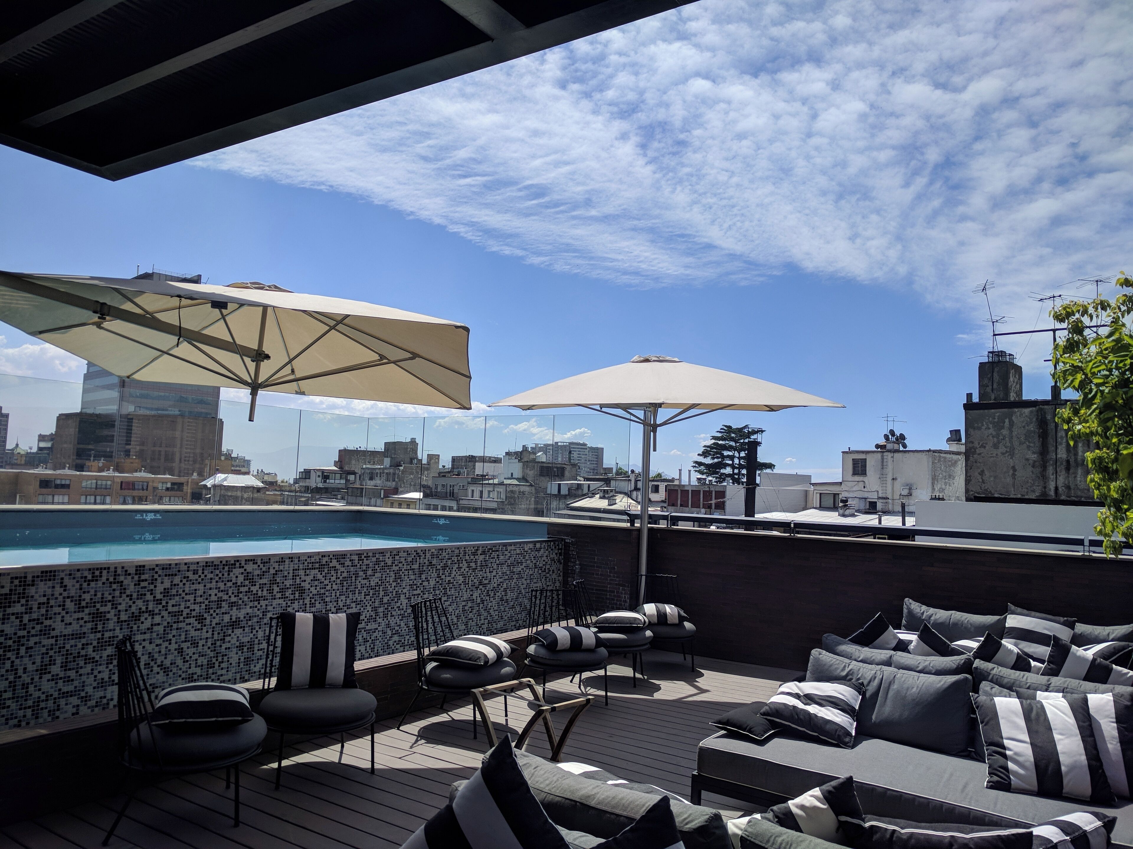 A rooftop pool area with lounge seating and umbrellas, overlooking a cityscape.