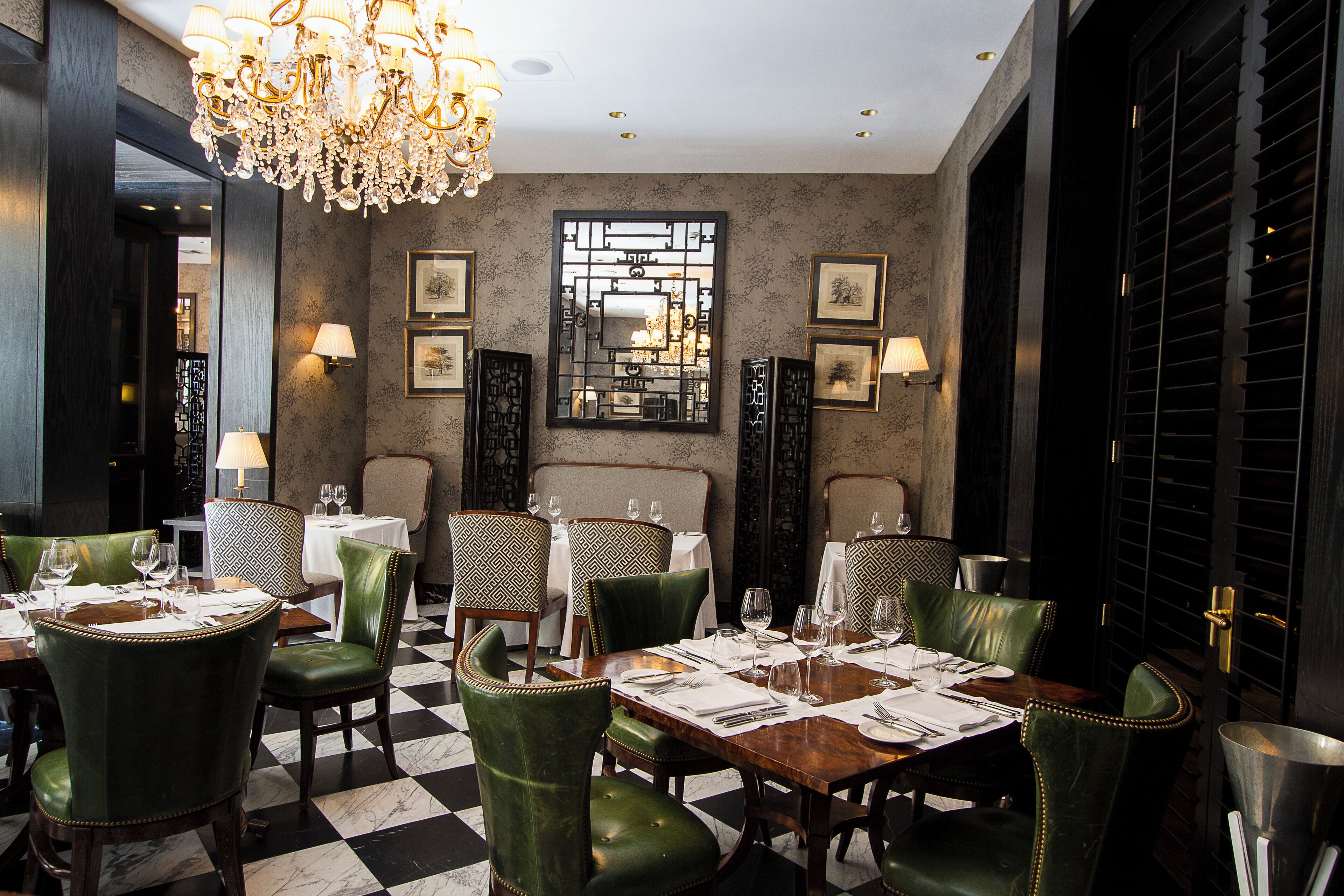 A dining area with green upholstered chairs, a chandelier, and framed artwork on the walls.