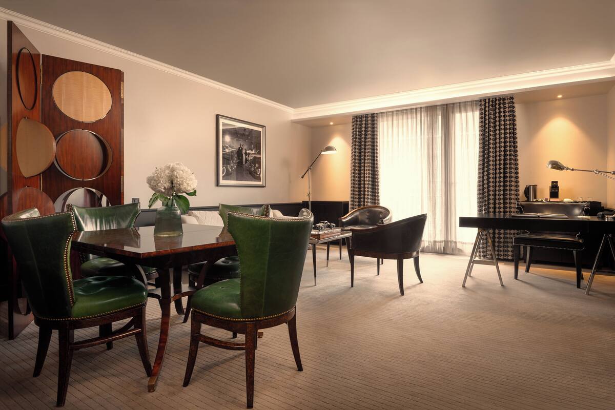 A hotel room with a dining area, a desk with a computer, and a large mirror.
