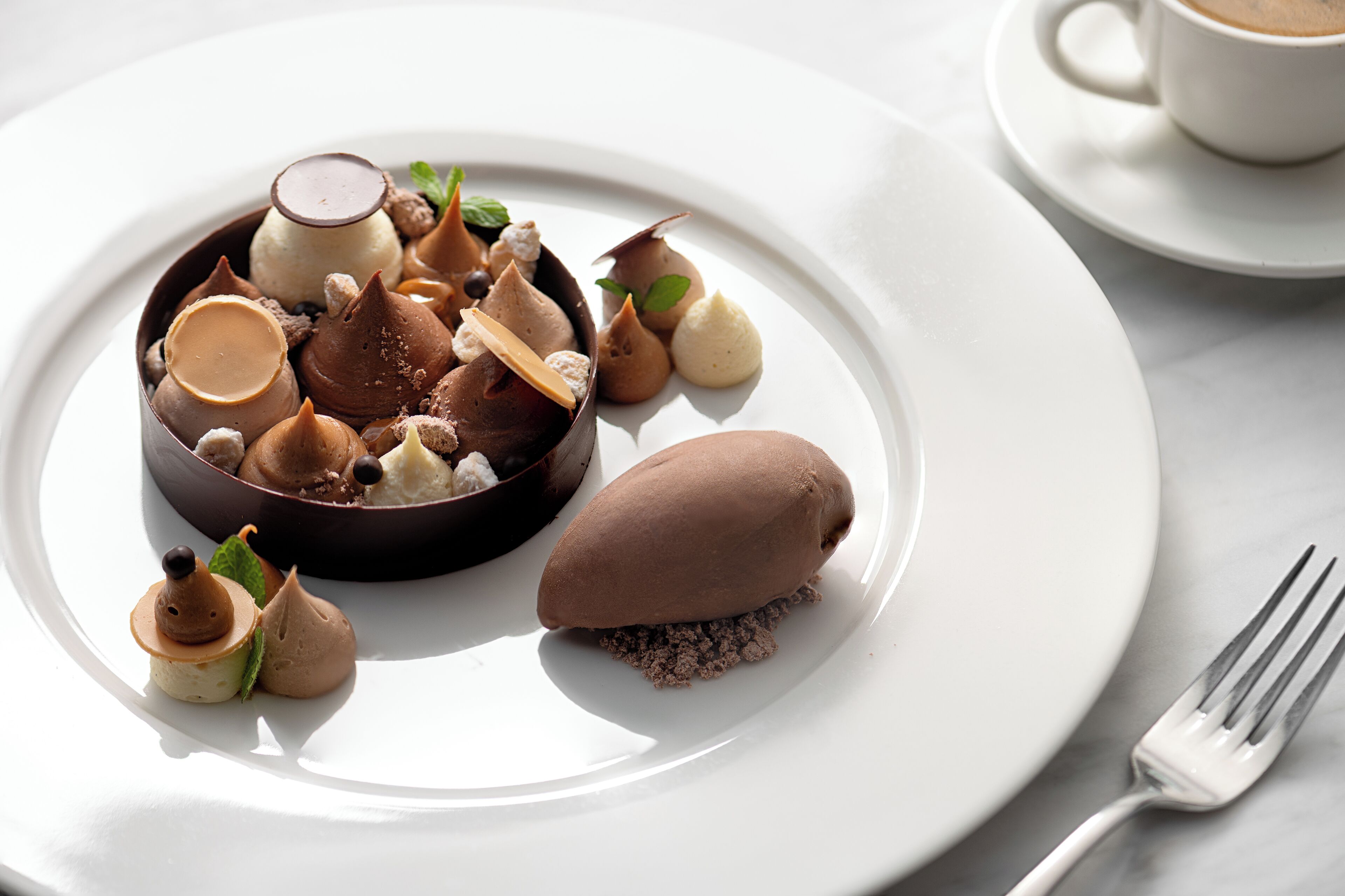 Une assiette à dessert contenant divers confiseries au chocolat et une tasse de café, le tout posé sur une table blanche.