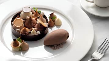 Une assiette à dessert contenant divers confiseries au chocolat et une tasse de café, le tout posé sur une table blanche.