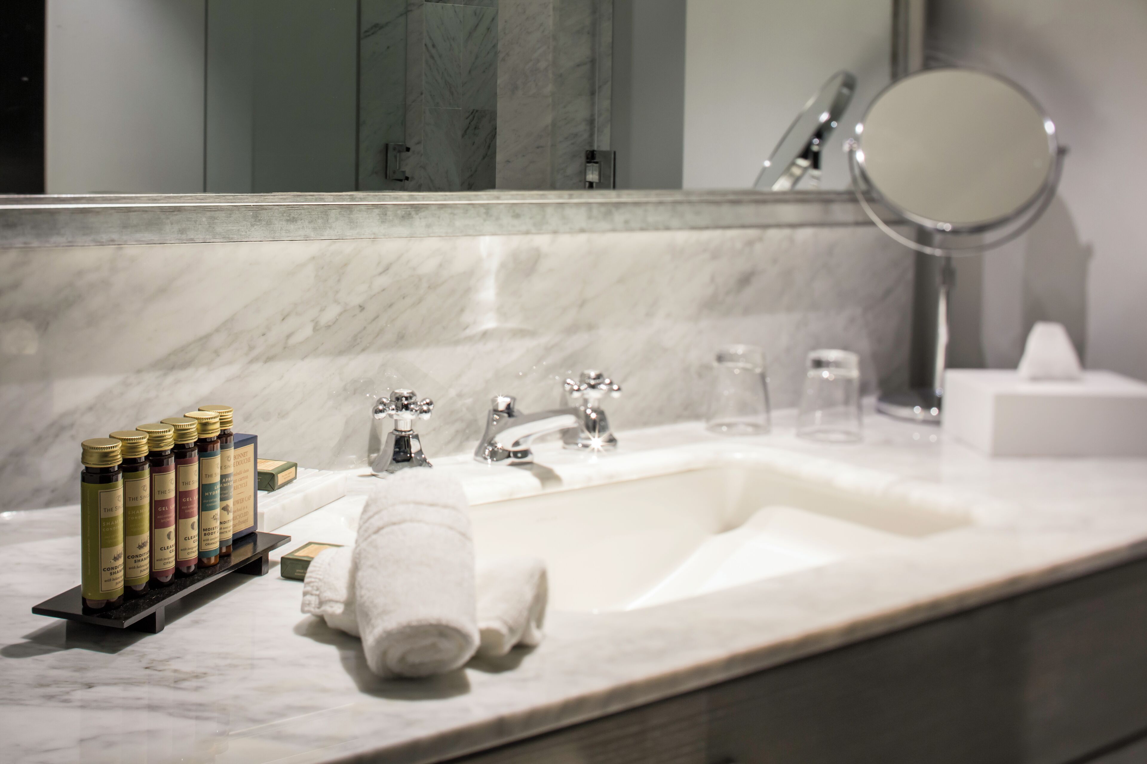 A bathroom with a marble sink, a mirror, and a shelf with toiletries.