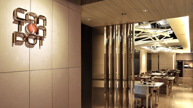 A modern restaurant interior with a central seating area, a decorative wall with a logo, and a contemporary ceiling design. - Lodgewood by Nina Hospitality丨Mong Kok (Kowloon)