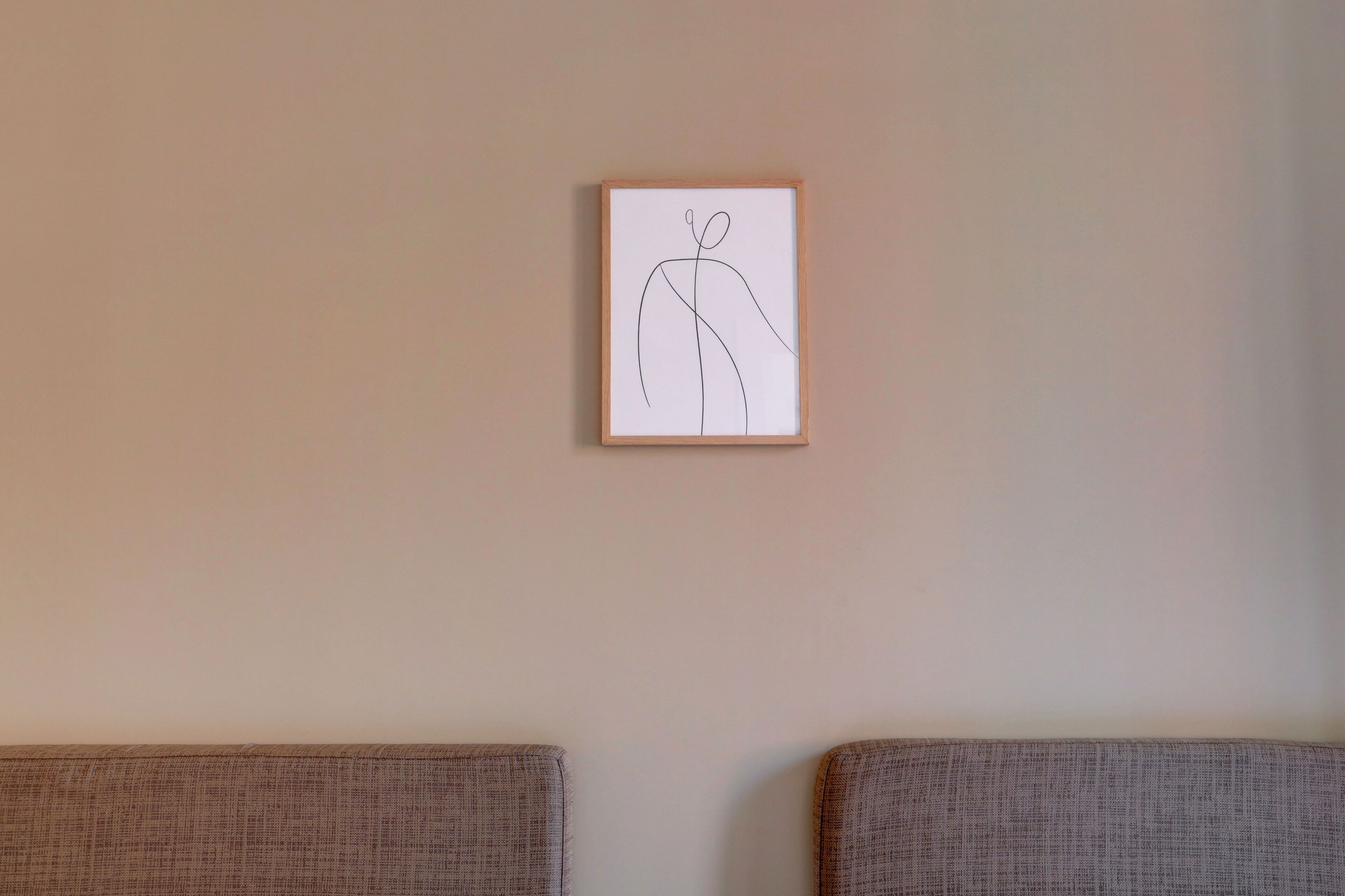 A framed line drawing on a plain wall, with two upholstered chairs in front.