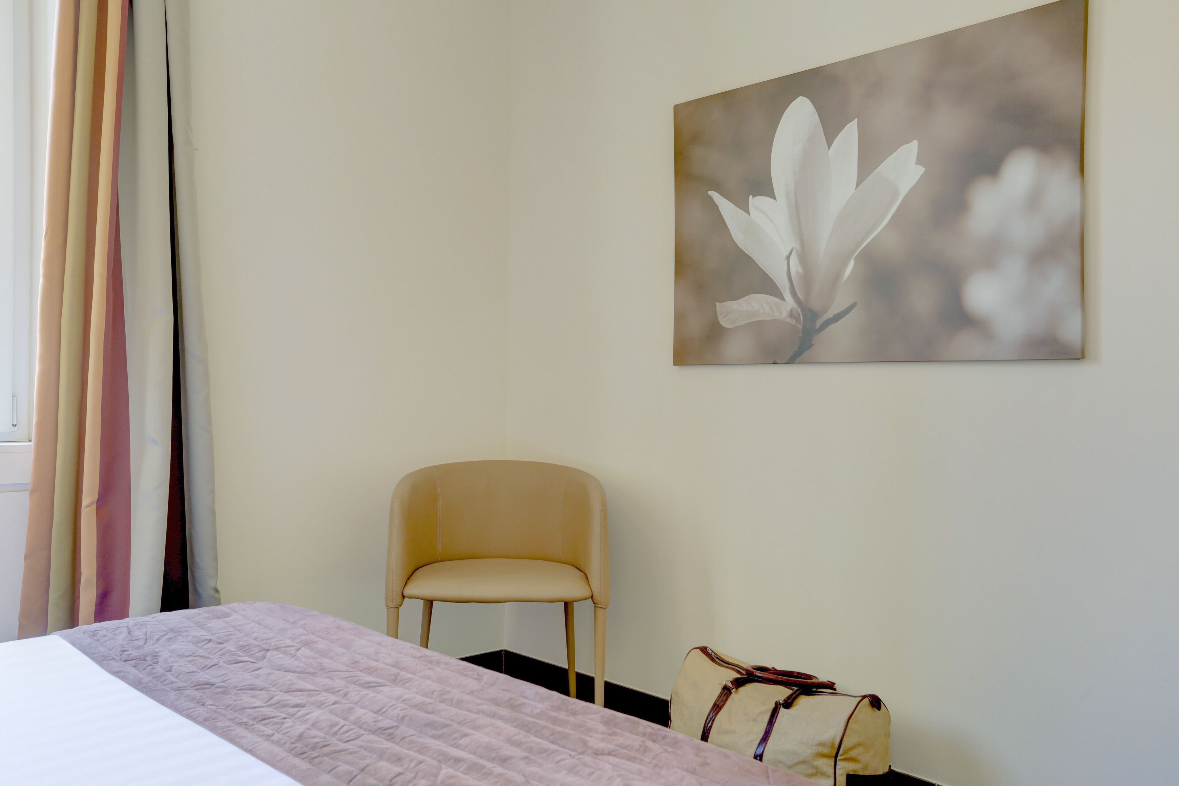 Une chambre d’hôtel avec un lit, une chaise, un tableau accroché au mur et une fenêtre avec des rideaux.