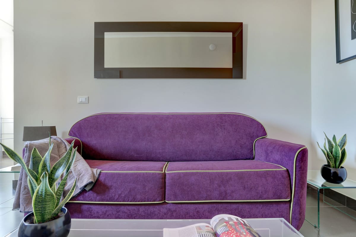 A purple sofa with green trim, a potted plant, and a magazine on a glass table.