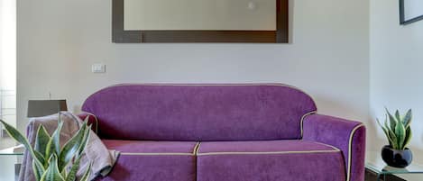 A purple sofa with green trim, a potted plant, and a magazine on a glass table.