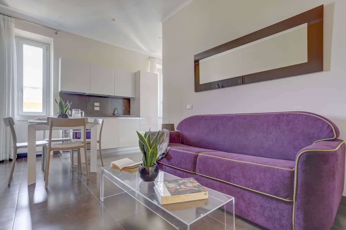 A modern living room with a purple sofa, a glass coffee table, and a dining area with a white table and chairs.