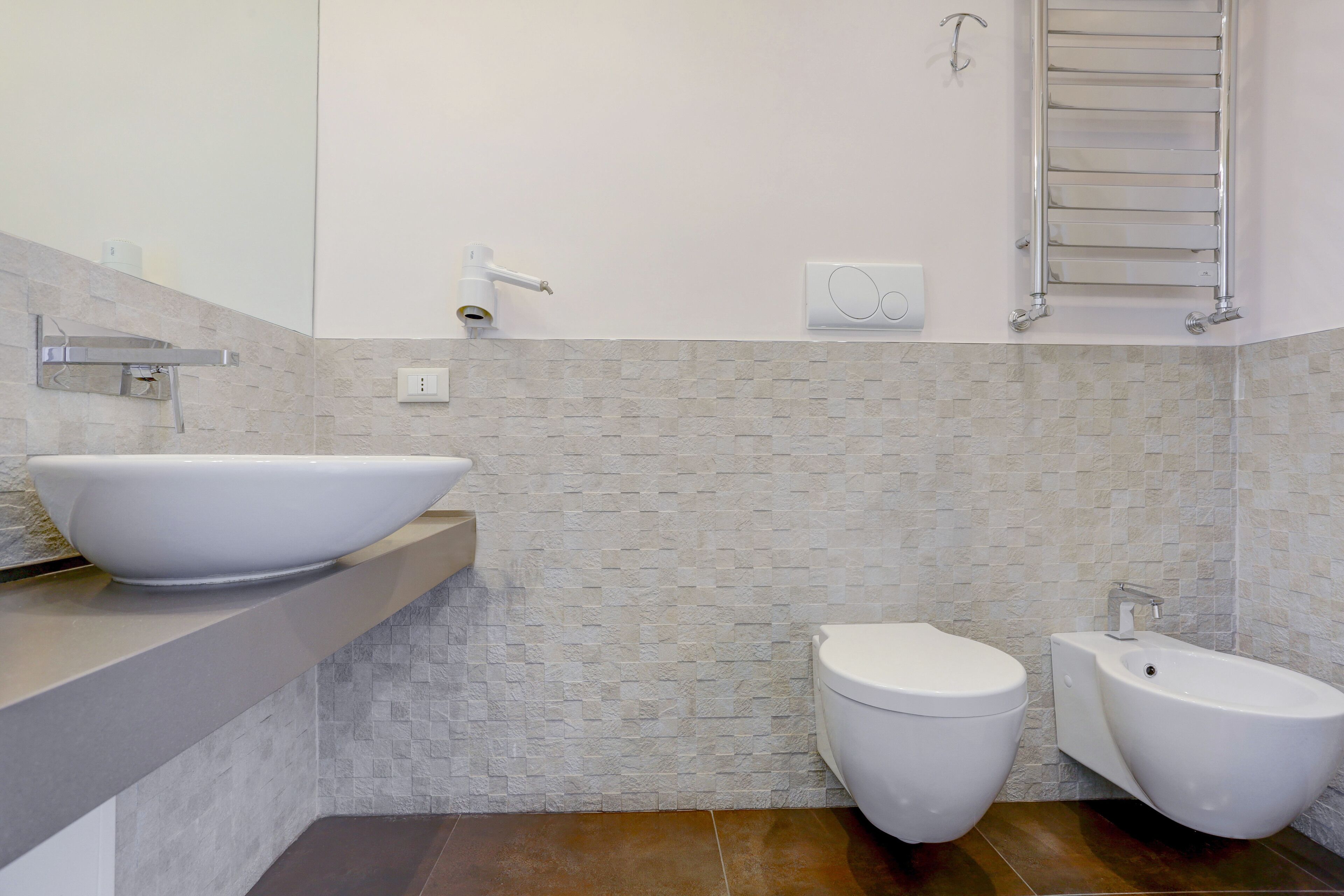A modern bathroom with a large white vessel sink, a toilet, and a bidet.
